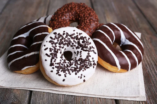 Deliciosos donuts com cobertura em guardanapo em fundo de madeira — Fotografia de Stock