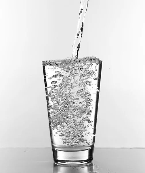 Νερό ρίχνει στο ποτήρι που απομονώνονται σε λευκό — Φωτογραφία Αρχείου