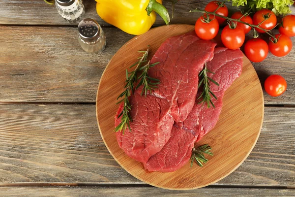 Bistecca di manzo cruda sul tagliere con verdure e spezie su fondo di legno — Foto Stock