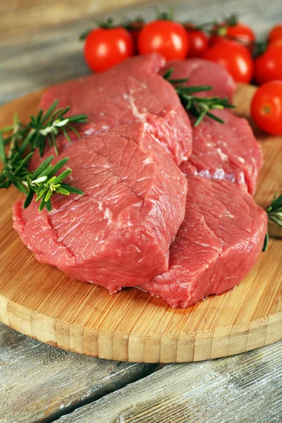 Biberiye ve domates ahşap arka plan üzerinde kesme tahtası üzerinde ham sığır eti biftek — Stok fotoğraf