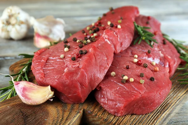 Syrové hovězí steak s rozmarýnem a česnekem na prkénko na dřevěné pozadí — Stock fotografie