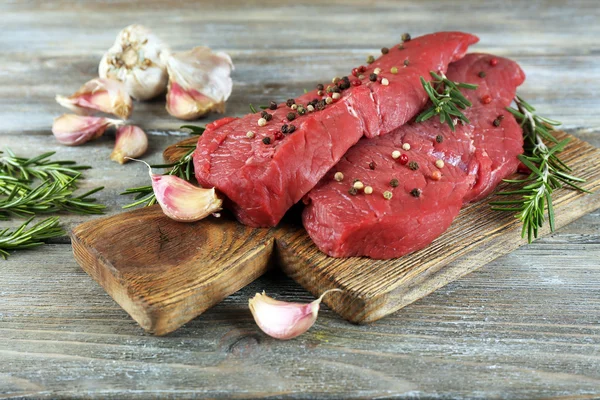 Rohes Rindersteak mit Rosmarin und Knoblauch auf Schneidebrett auf Holzgrund — Stockfoto