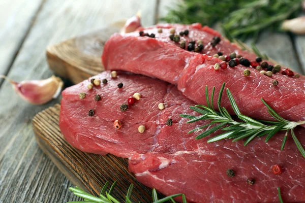 Steak daging sapi mentah dengan rosemary dan bawang putih pada potongan papan pada latar belakang kayu — Stok Foto