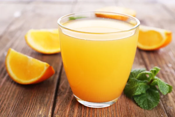 Стакан апельсинового сока с апельсинами на деревянном столе — стоковое фото