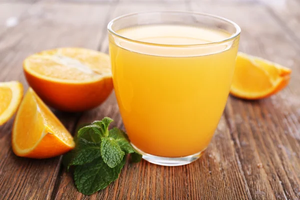 Glas apelsinjuice med apelsiner på träbord nära håll — Stockfoto