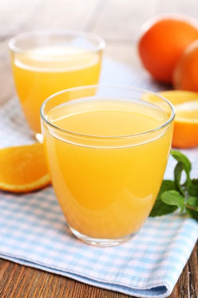 Стаканы апельсинового сока с апельсинами на деревянном столе — стоковое фото