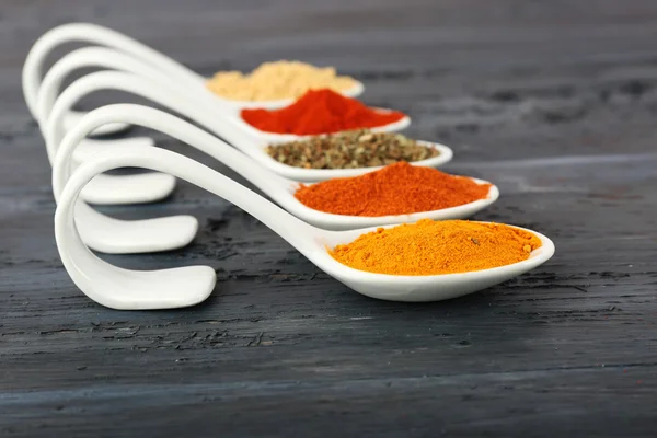 Different kinds of spices in spoons on wooden background — Stock Photo, Image