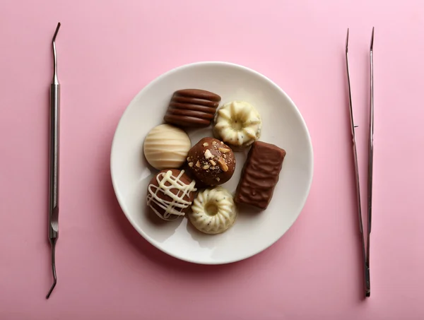 Tandläkare verktyg med godis på plattan på rosa bakgrund — Stockfoto