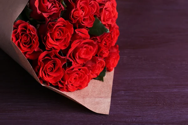 Bouquet de roses rouges enveloppé dans du papier sur fond de bois — Photo