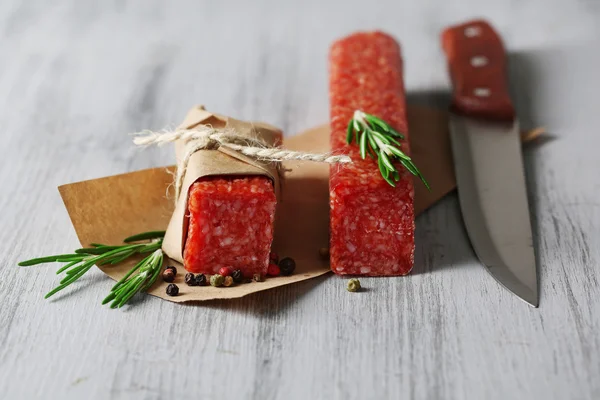 Salsicha de salame saborosa, sobre papel sobre fundo de madeira — Fotografia de Stock