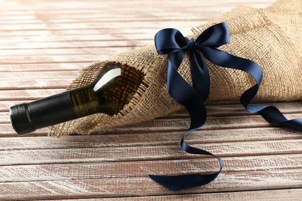 Wine bottle wrapped in burlap cloth on wooden planks background — Stock Photo, Image