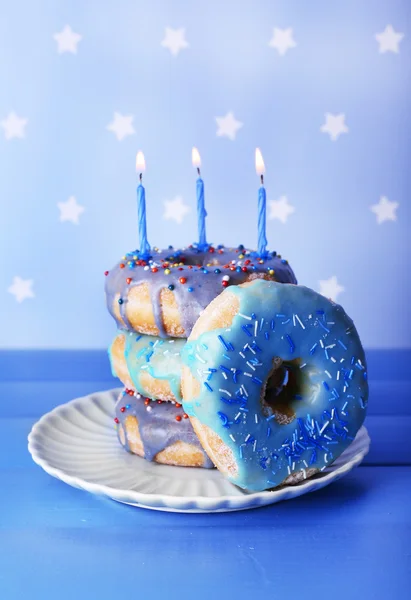 Deliciosas rosquillas con glaseado y velas de cumpleaños en la mesa sobre fondo brillante — Foto de Stock