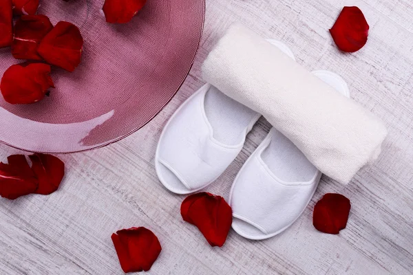 Spa bowl with water, rose petals, towel and slippers on light background. Concept of pedicure or natural spa treatment — Stock Photo, Image