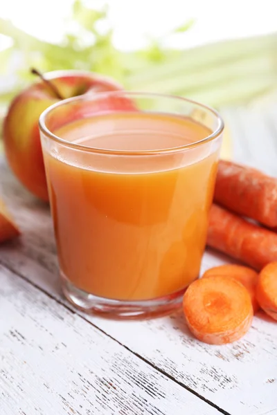 Glass of juice with apple and carrot on wooden table close up