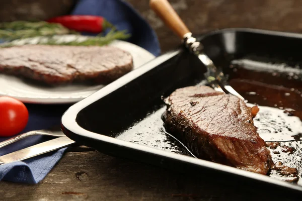 Composição com carne assada saborosa em panela, tomates e raminhos de alecrim em fundo de madeira — Fotografia de Stock