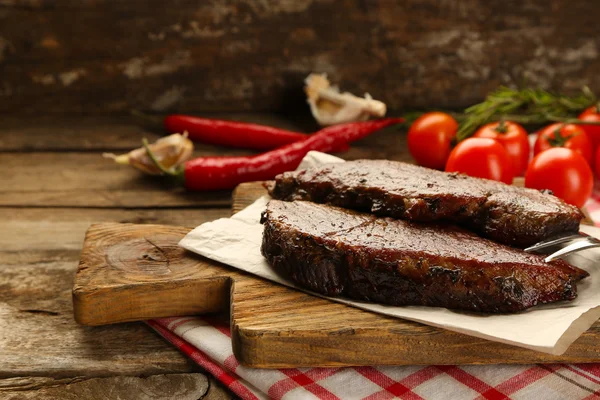 Composition with tasty roasted meat on cutting board, tomatoes and rosemary sprigs on wooden background — Stock Photo, Image