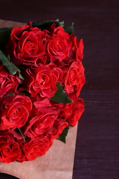 Ramo de rosas rojas envueltas en papel sobre fondo de madera — Foto de Stock