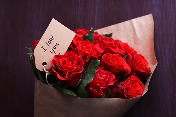 Ramo de rosas rojas con etiqueta envuelta en papel sobre fondo de madera —  Fotos de Stock