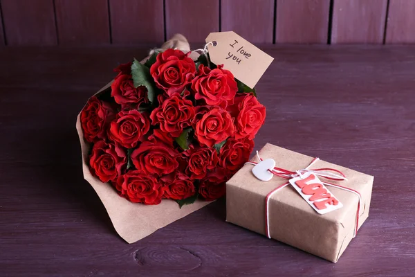 Bouquet de roses rouges enveloppé dans du papier et boîte cadeau sur fond de bois — Photo