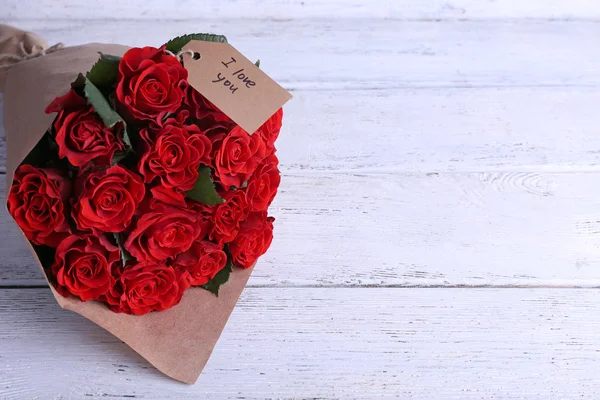 Ramo de rosas rojas con etiqueta envuelta en papel sobre fondo de madera —  Fotos de Stock