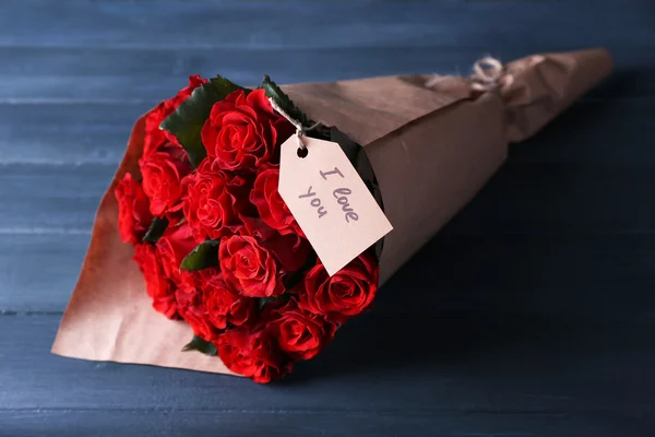 Ramo de rosas rojas con etiqueta envuelta en papel sobre fondo de madera — Foto de Stock