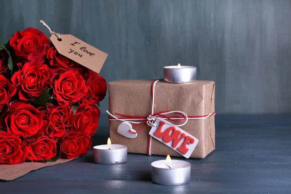 红玫瑰花束裹在纸，礼品盒，木制背景上的蜡烛 — 图库照片