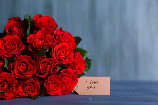 Ramo de rosas rojas con etiqueta sobre fondo de madera — Foto de Stock