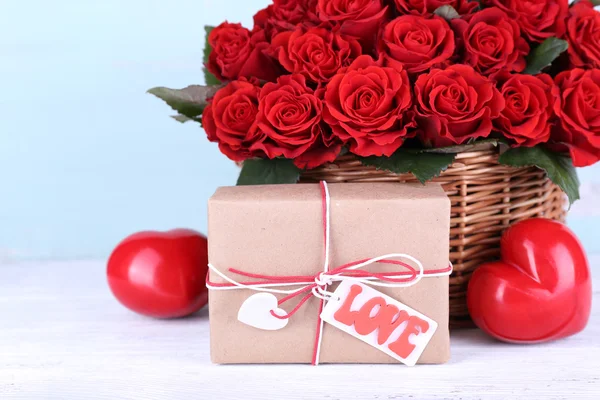 Bouquet of red roses in basket with present box on wooden background — Stock Photo, Image