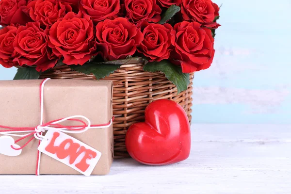 Bouquet of red roses in basket with present box on wooden background — Stock Photo, Image
