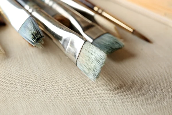 Different paintbrushes on fabric background — Stock Photo, Image