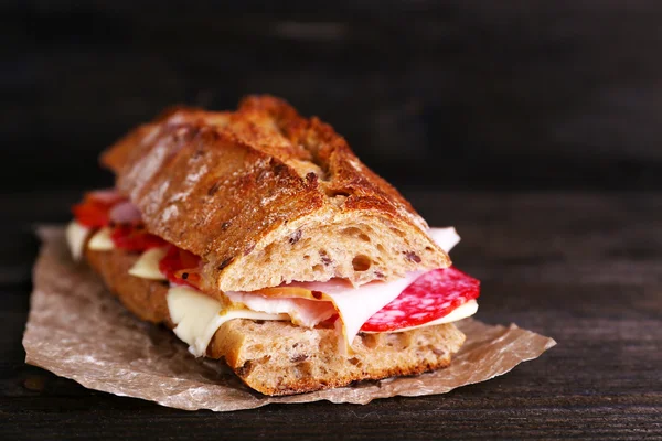 Fresh and tasty sandwich with ham and cheese on paper on wooden background — Stock Photo, Image