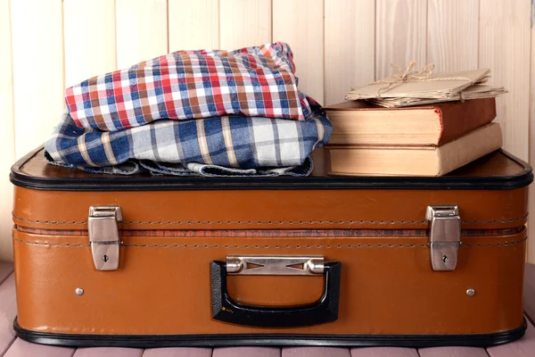 Maleta vintage con ropa y libros sobre fondo de madera — Foto de Stock