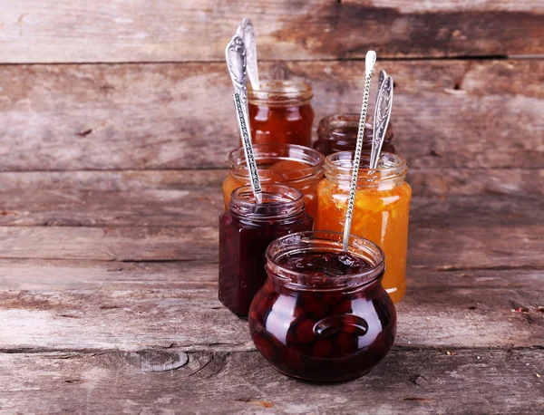 Gläser mit schmackhafter Marmelade auf hölzernem Hintergrund — Stockfoto