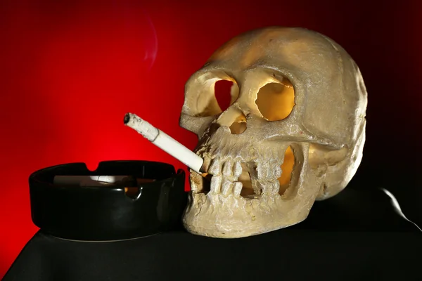 Smoking human scull with cigarette in his mouth on dark color background — Stock Photo, Image