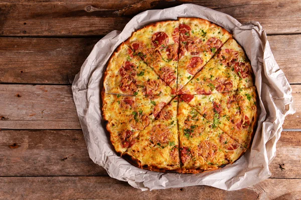 Pizza saborosa em papel sobre fundo de madeira — Fotografia de Stock