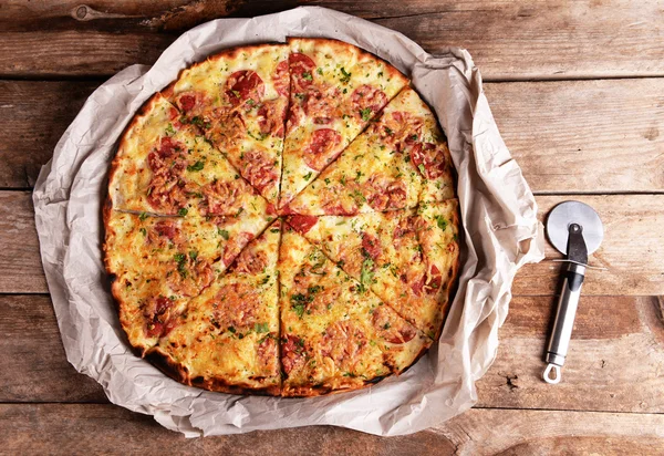 Pizza saborosa em papel sobre fundo de madeira — Fotografia de Stock