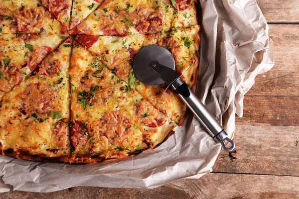 Tasty pizza on paper with knife on wooden background — Stock Photo, Image