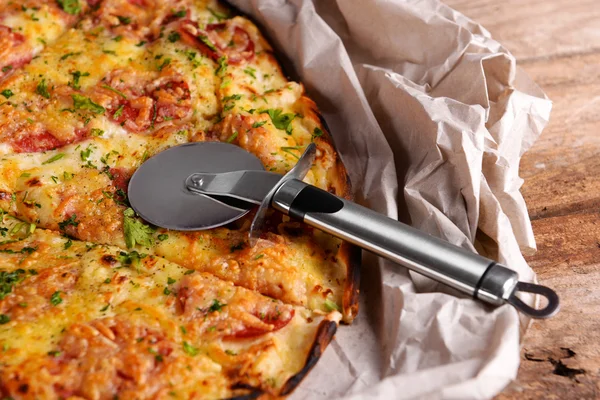 Tasty pizza on paper with knife on wooden background — Stock Photo, Image