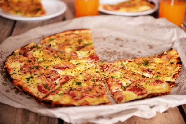 Smakelijke pizza op papier met glazen SAP op tafel close-up — Stockfoto