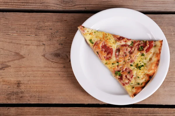 Tasty slice of pizza on plate on wooden table — Stock Photo, Image