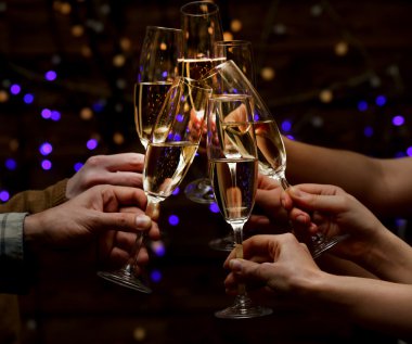 Clinking glasses of champagne in hands on bright lights background clipart