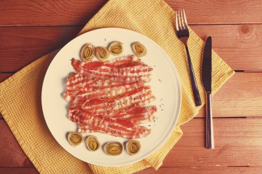 Dilimleri soğancık ile peçete ahşap masa arka plan üzerinde beyaz plaka ile pastırma şeritler