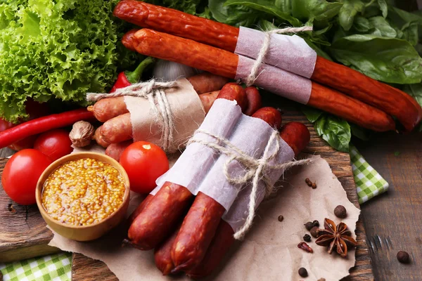 Surtido de salchichas finas, mostaza en tazón y especias en tabla de cortar, sobre fondo de madera — Foto de Stock