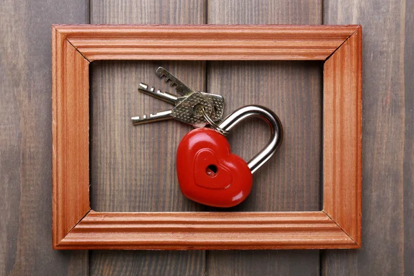 Heart-shaped padlock with key on wooden background