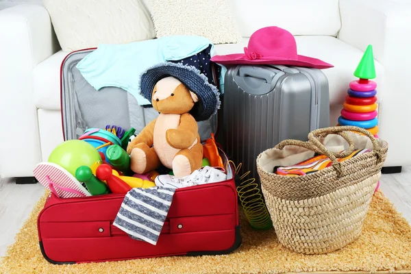 Koffer voller Kleidung und Kinderspielzeug auf Fellteppich und weißem Sofa-Hintergrund — Stockfoto