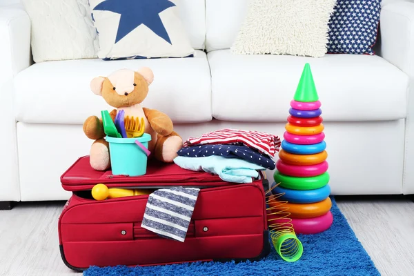 Suitcase packed with clothes and child toys on fur rug and white sofa background — Stock Photo, Image