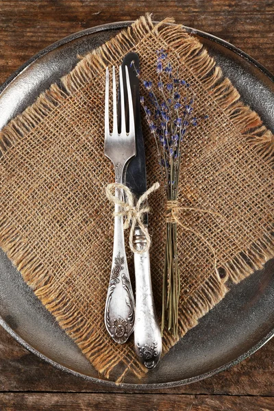 Platería atada con cuerda en bandeja metálica con tela de arpillera y flor seca sobre fondo de madera — Foto de Stock