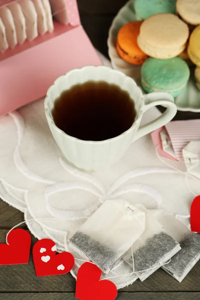 Heart shaped teabag tags, macaroons and cup of tea on wooden background — Stock Photo, Image