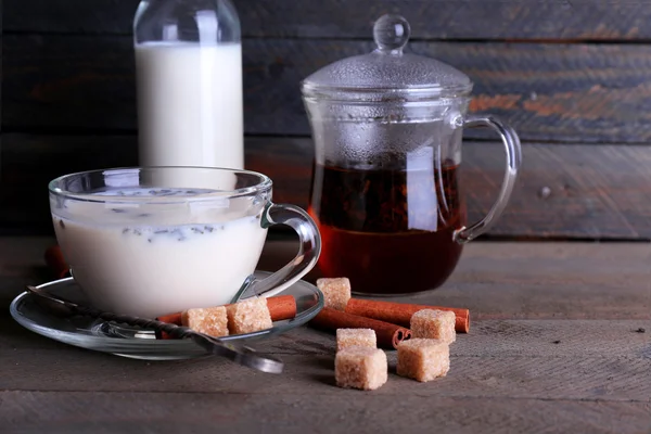 Té negro con leche en cristalería y azúcar en terrón sobre fondo de tablones de madera de color — Foto de Stock