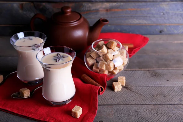 Chá preto com leite em copos e bule com açúcar de caroço na cor pranchas de madeira fundo — Fotografia de Stock